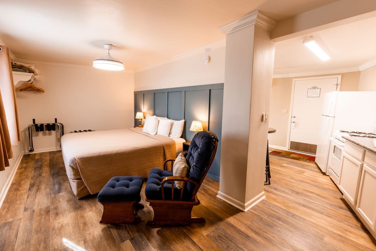 A hotel room with a large bed, a chair, a desk, and a kitchenette.