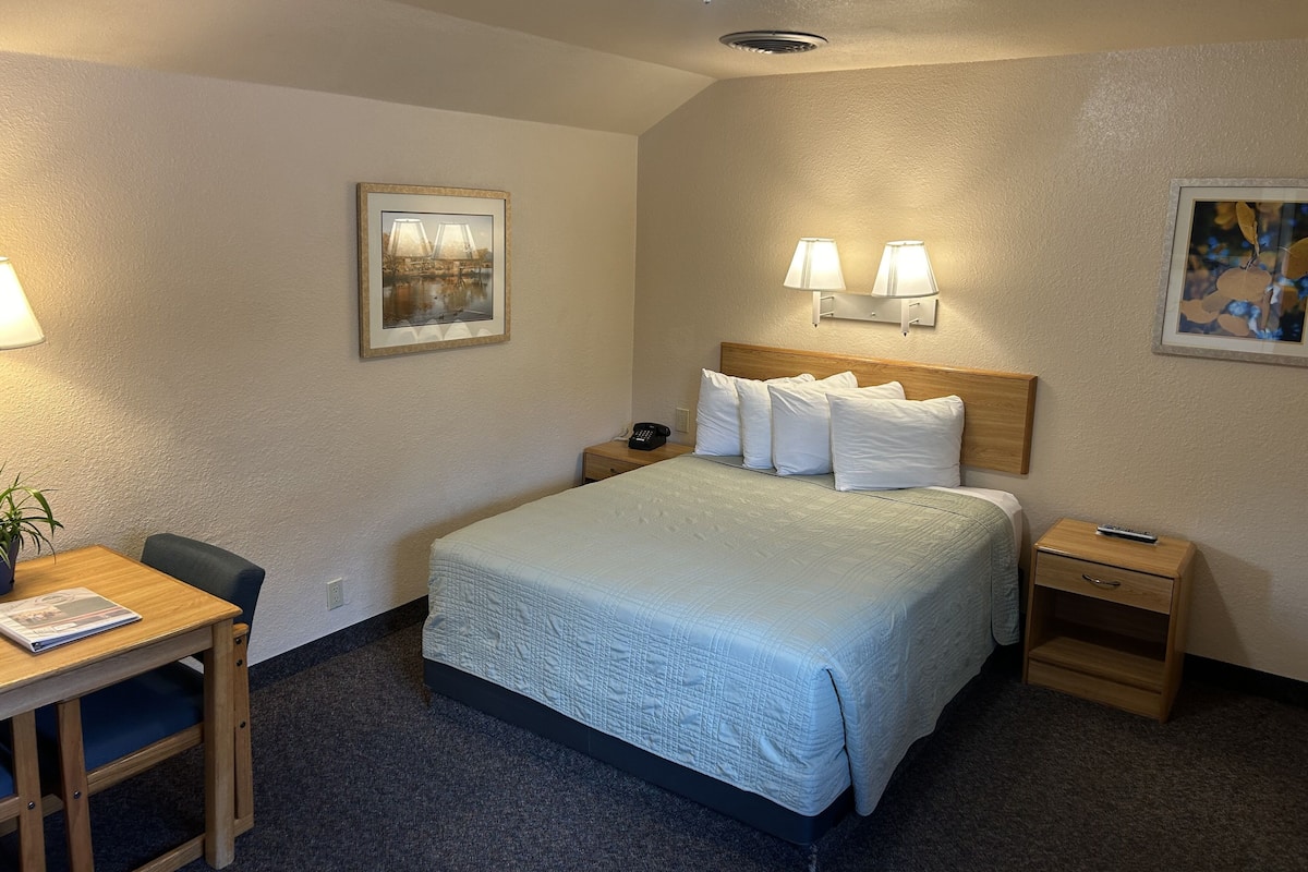 A hotel room with a bed, bedside tables, a desk with a chair, and two wall-mounted lamps.