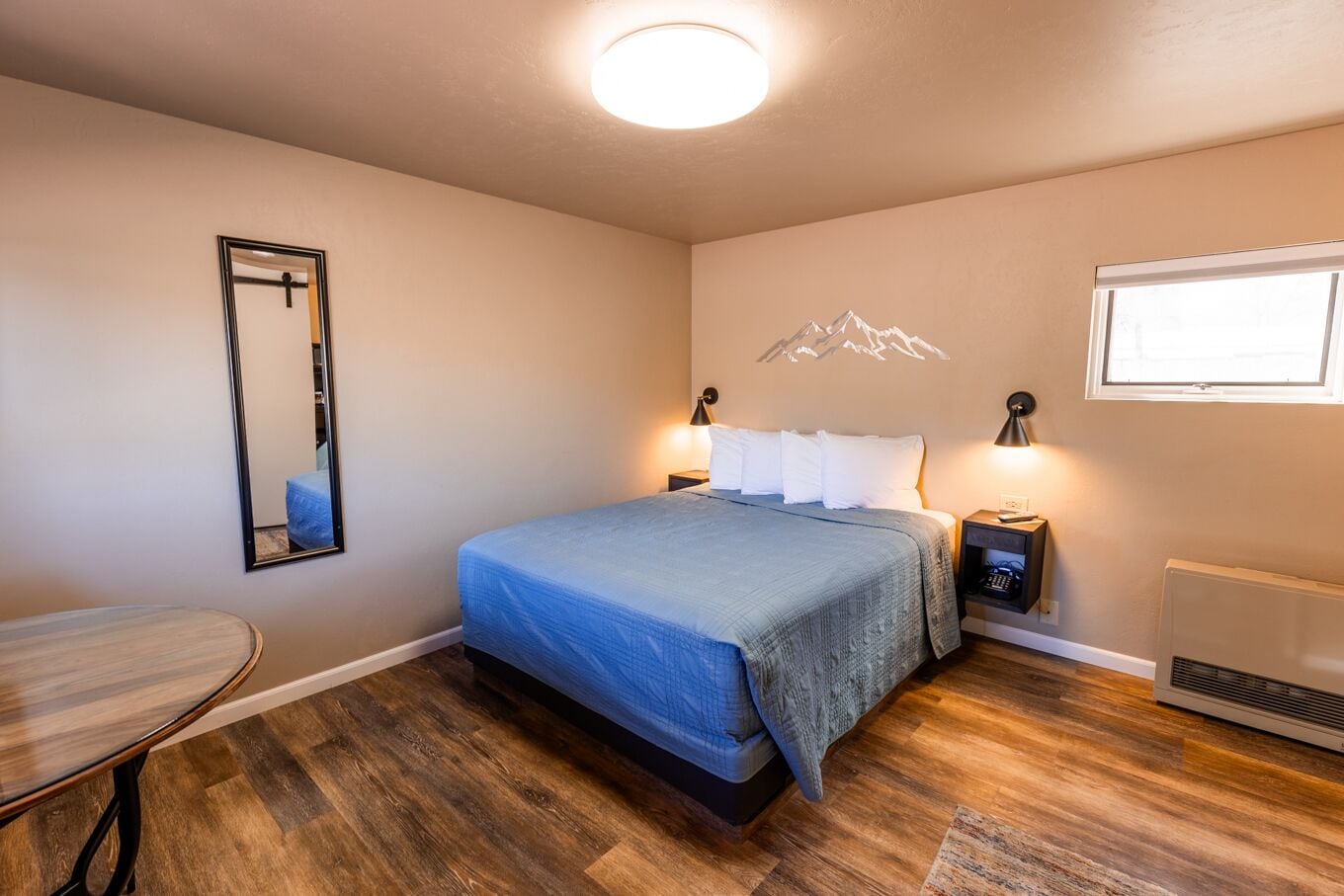 A bedroom with a bed, bedside tables, a mirror, a heater, and a window.