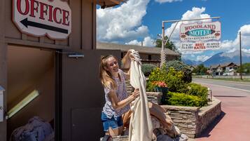 A motel sign with amenities listed, a laundry cart outside, and a clear sky.