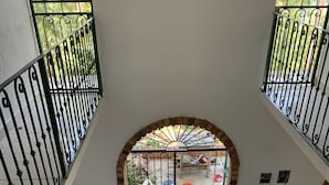 Un espace intérieur spacieux doté d’un sol carrelé, d’une cuisine avec un évier et un plan de travail, et d’une vue sur un jardin extérieur, accessible par un passage en arc de cercle.