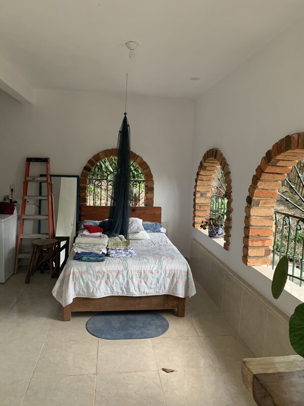 A bedroom with a bed, a ladder, a chair, and a large window with a view of greenery. - CASAS LAS PAROTAS - 3 BR, 2 Bath home, on hillside overlooking Yelapa Bay (Yelapa)