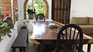 Un coin repas comprenant une table en bois, deux chaises, un banc et un mur en briques surmonté d’une arche.