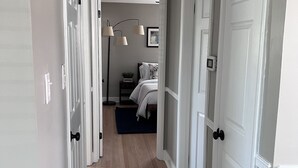 Un couloir avec un plancher en bois, des portes blanches et, au fond, un lit doté d’une tête de lit sombre.
