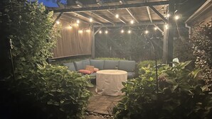 Un espace extérieur aménagé en terrasse, doté d’un coin salon couvert, de guirlandes lumineuses et d’une végétation luxuriante.