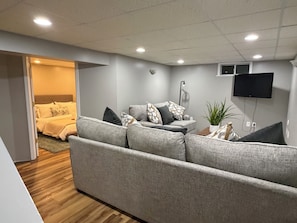 A modern living room with a grey sofa, a flat-screen TV mounted on the wall, and a wooden floor. - Boho Chic Cape (Albany)