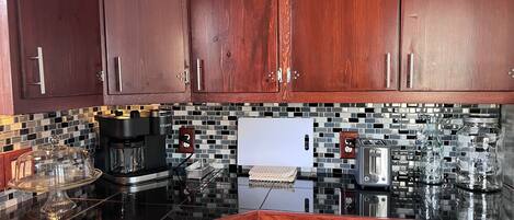 A kitchen with dark wooden cabinets, a tiled backsplash, and modern appliances including a coffee maker, toaster, and kettle.