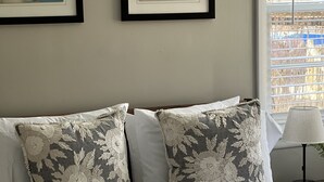 Un lit bien fait, agrémenté d’oreillers à motifs floraux et recouvert d’une courtepointe blanche. Deux œuvres d’art encadrées sont accrochées au-dessus du lit.