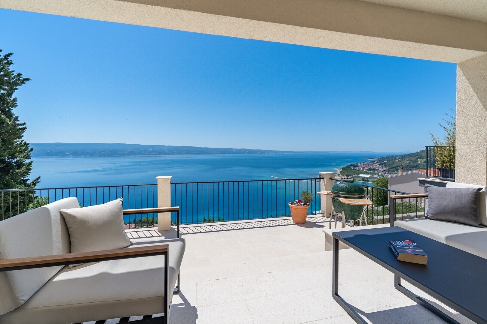 A balcony with a view of the sea, outdoor furniture, and a grill.