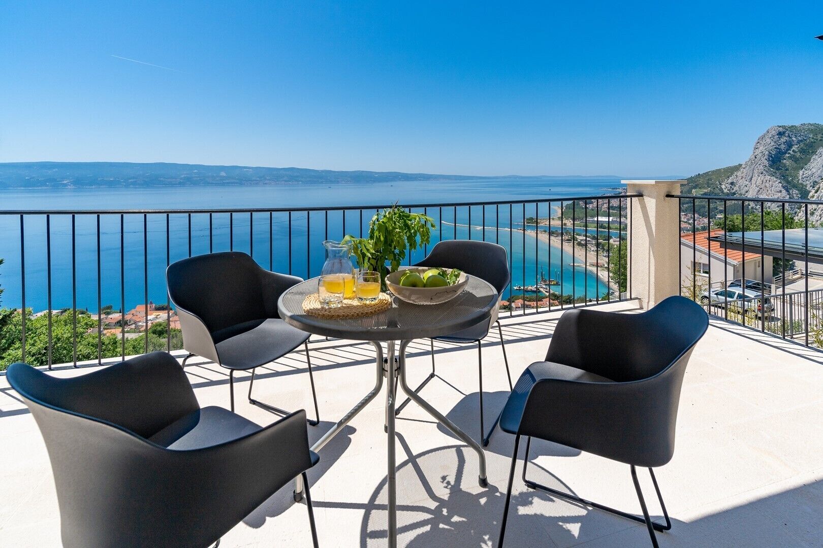 Un balcon avec une table, des chaises et une vue sur la mer et les montagnes.