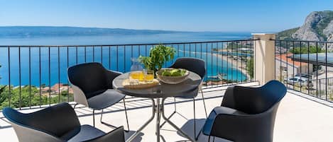 Un balcon avec une table, des chaises et une vue sur la mer et les montagnes.