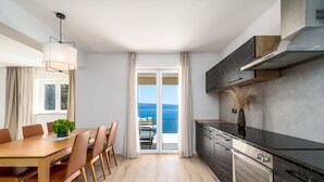 A modern kitchen with a view of the sea, a dining area with a table and chairs, and a large window with curtains. - New! Villa Atopos with heated private pool, 5 bedrooms, Cinema room, panoramic sea views (Omis)