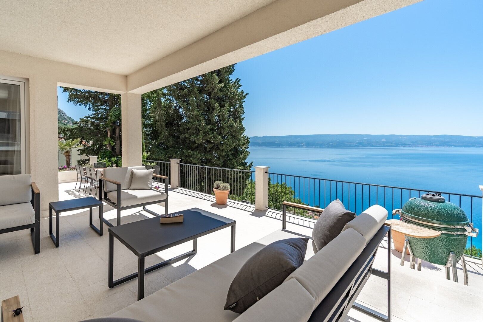 Ein Balkon mit einer Couch, Stühlen und einem Tisch, der einen malerischen Blick auf ein Gewässer und Berge bietet.