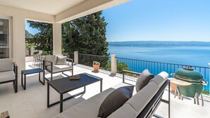 A balcony with a sofa, chairs, and a table, overlooking a scenic view of a body of water and mountains. - New! Villa Atopos with heated private pool, 5 bedrooms, Cinema room, panoramic sea views (Omis)