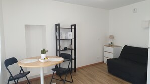 Ein modernes Wohnzimmer mit einem runden Tisch, zwei Stühlen, einem schwarzen Sofa, einem Bücherregal und einem kleinen Beistelltisch mit einer Lampe.