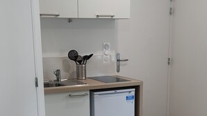 Eine kleine Küche mit weißen Schränken, einem integrierten Geschirrspüler und einem Mülleimer.