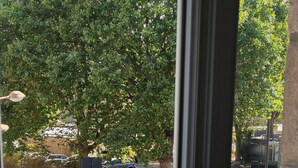 Blick durch ein Fenster mit Metallgitter auf einen Parkplatz und Bäume im Hintergrund.
