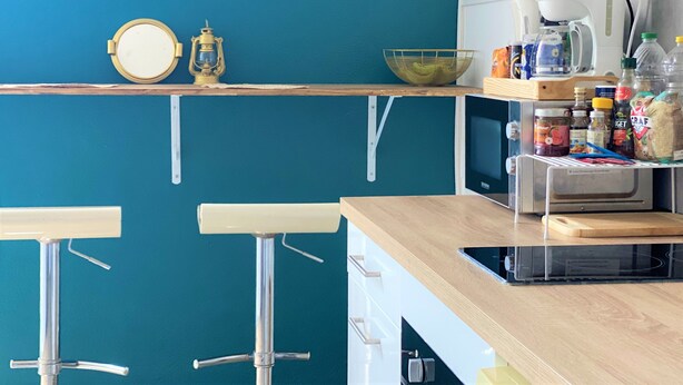 Een keuken met een blauwe wand, een klok, een koffiezetapparaat en barstoelen.