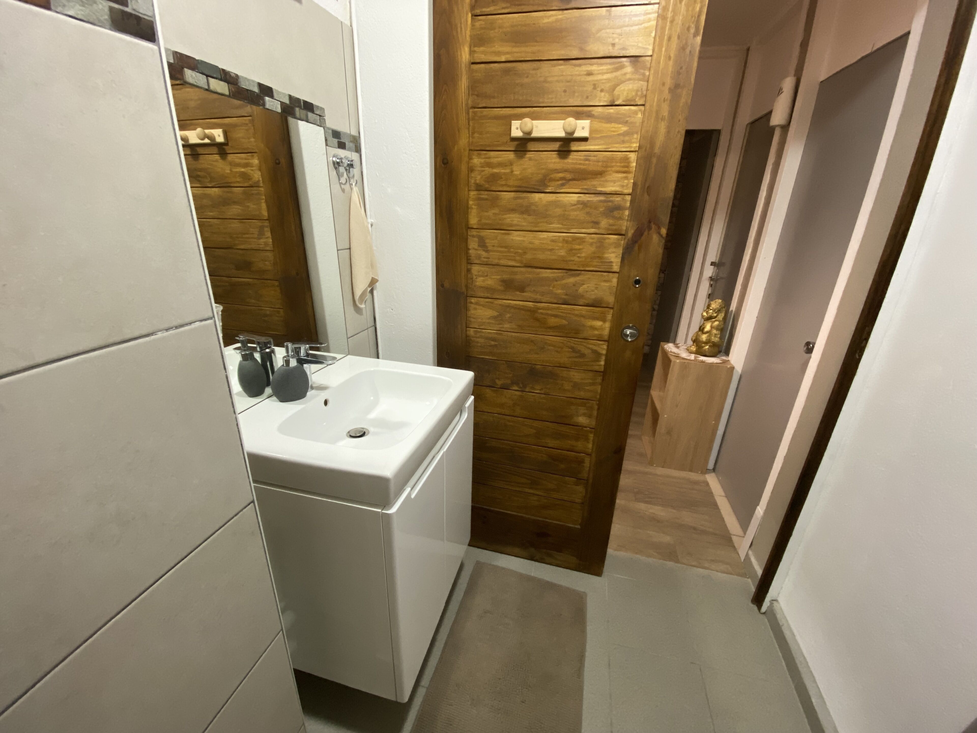 Une salle de bain avec un lavabo blanc, un miroir et une porte en bois.