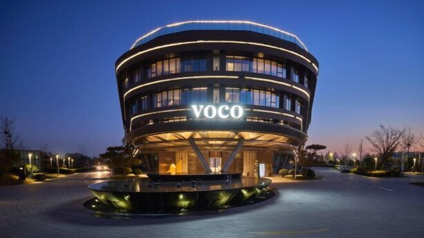 Um edifício moderno com design circular e o nome "VOCO" iluminado na fachada.