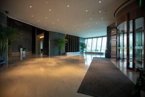 Eine geräumige Lobby mit glänzendem Boden, großen Fenstern und Zimmerpflanzen.