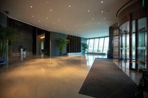 A spacious lobby with a polished floor, large windows, and potted plants.
