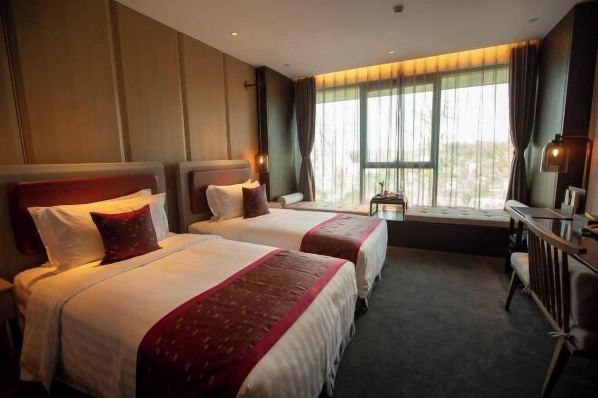 Een hotelkamer met twee bedden, een bureau en een raam met gordijnen.