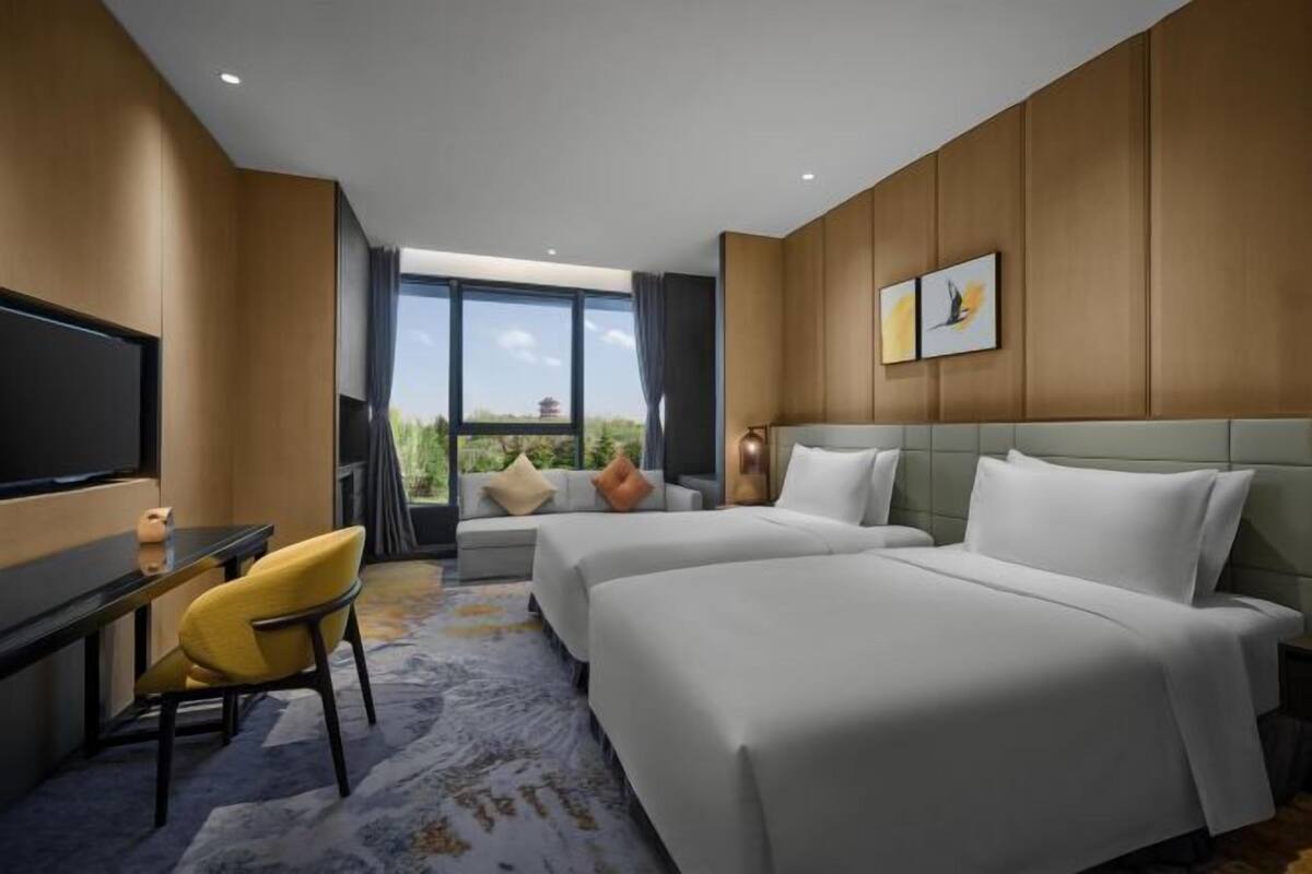 Hotelkamer met twee bedden, een televisie, bureau en groot raam met uitzicht op groen.