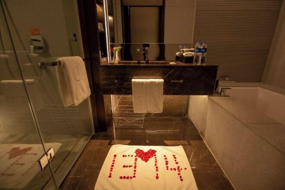 Ein modernes Badezimmer mit Duschkabine aus Glas, einer dunklen Marmorarbeitsplatte und einem weißen Handtuch auf dem Boden.