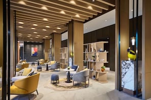 A modern lobby with seating areas, bookshelves, and a marble reception desk. - voco ZHENGZHOU GARDEN EXPO by IHG (Xinzheng)