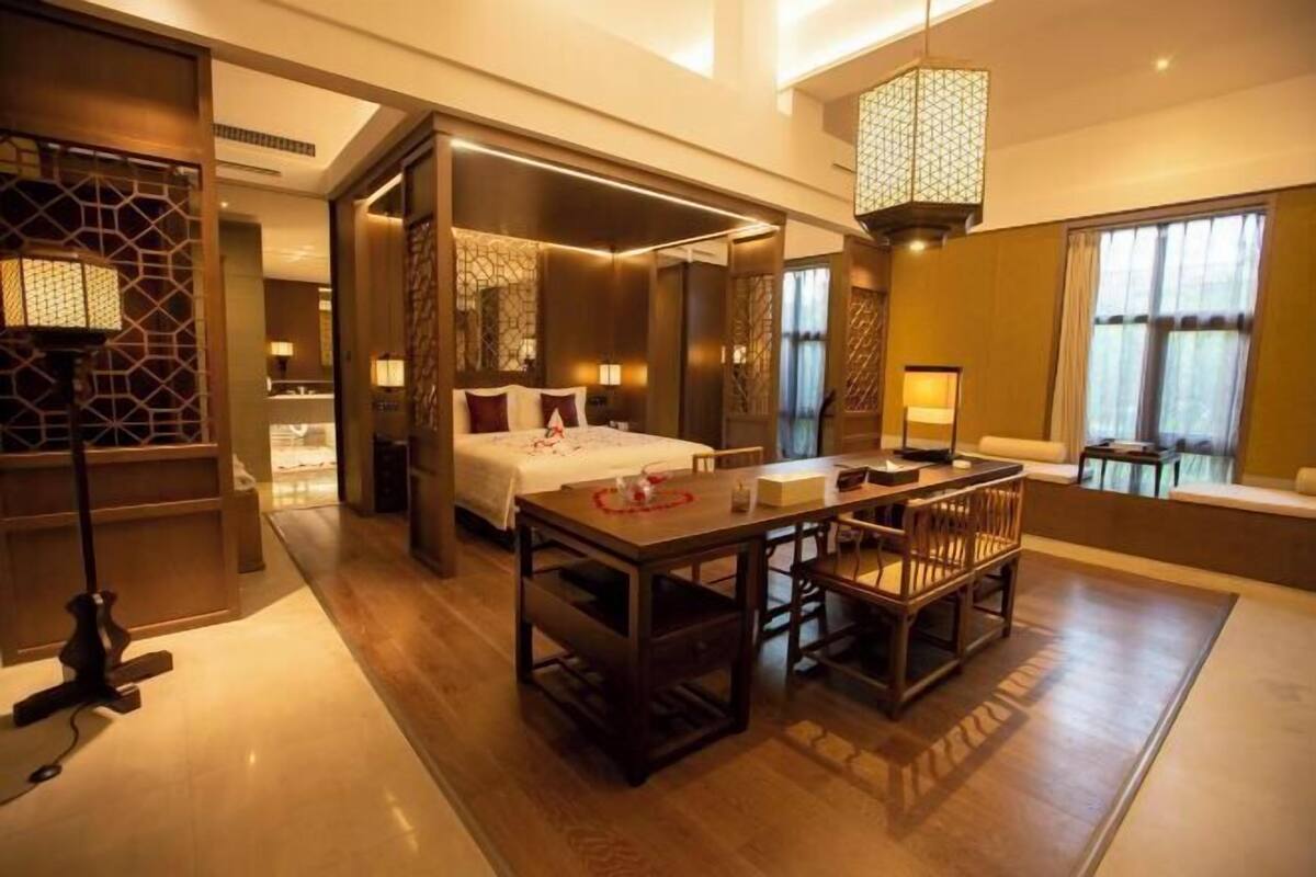 Een moderne hotelkamer met een groot bed, een zithoek met houten meubels en een groot raam met gordijnen.