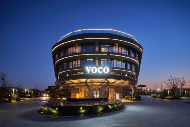 A modern building with a circular design, labeled 'VOCO,' featuring a central open space and a surrounding water feature.