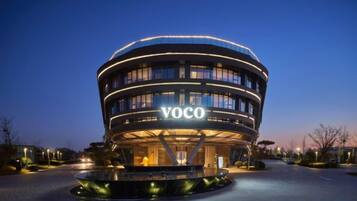 A modern building with a circular design, labeled 'VOCO,' featuring a central open space and a surrounding water feature.