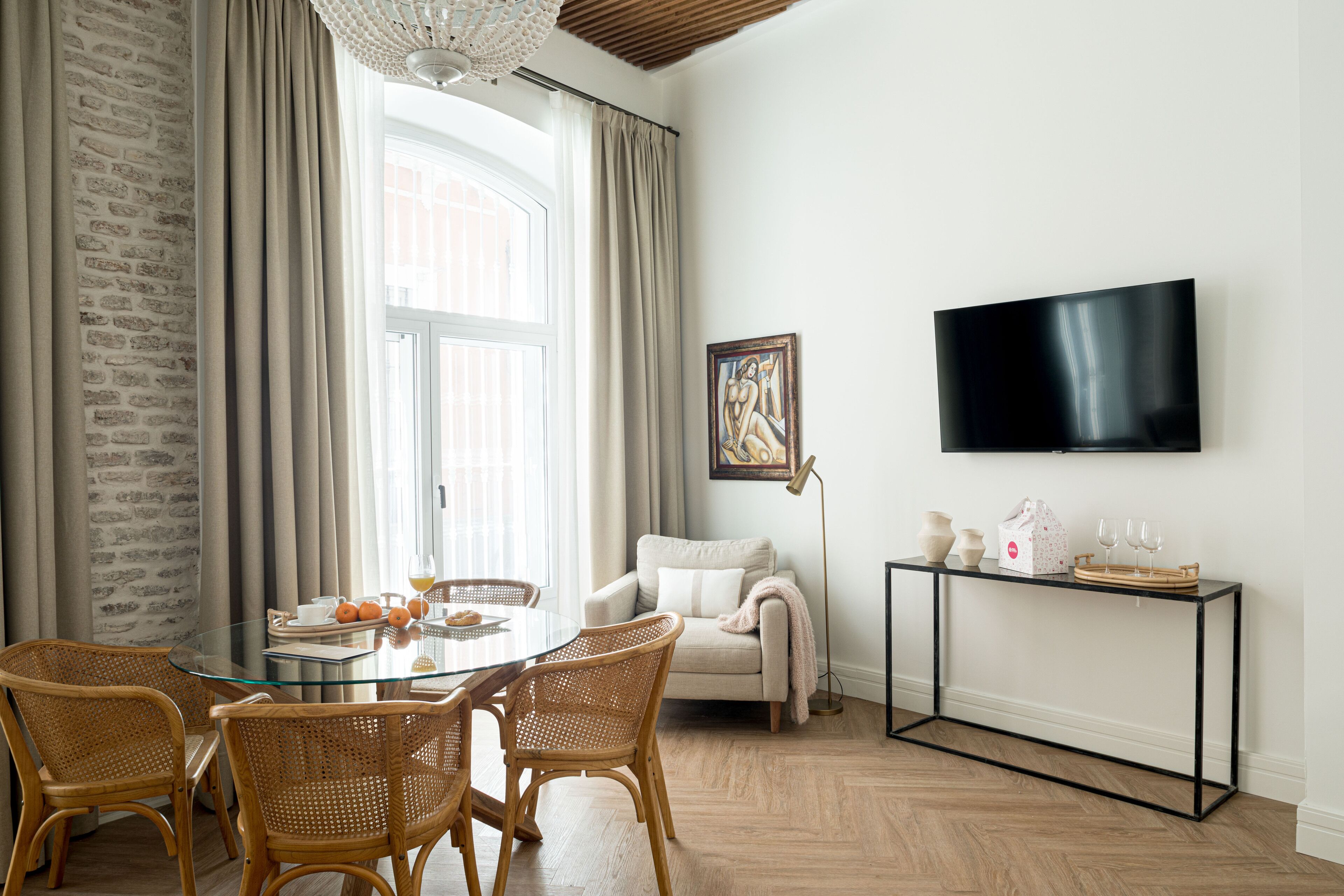 Een eetgedeelte met een glazen tafel, rieten stoelen, een witte bank en een televisie op een zwarte standaard.