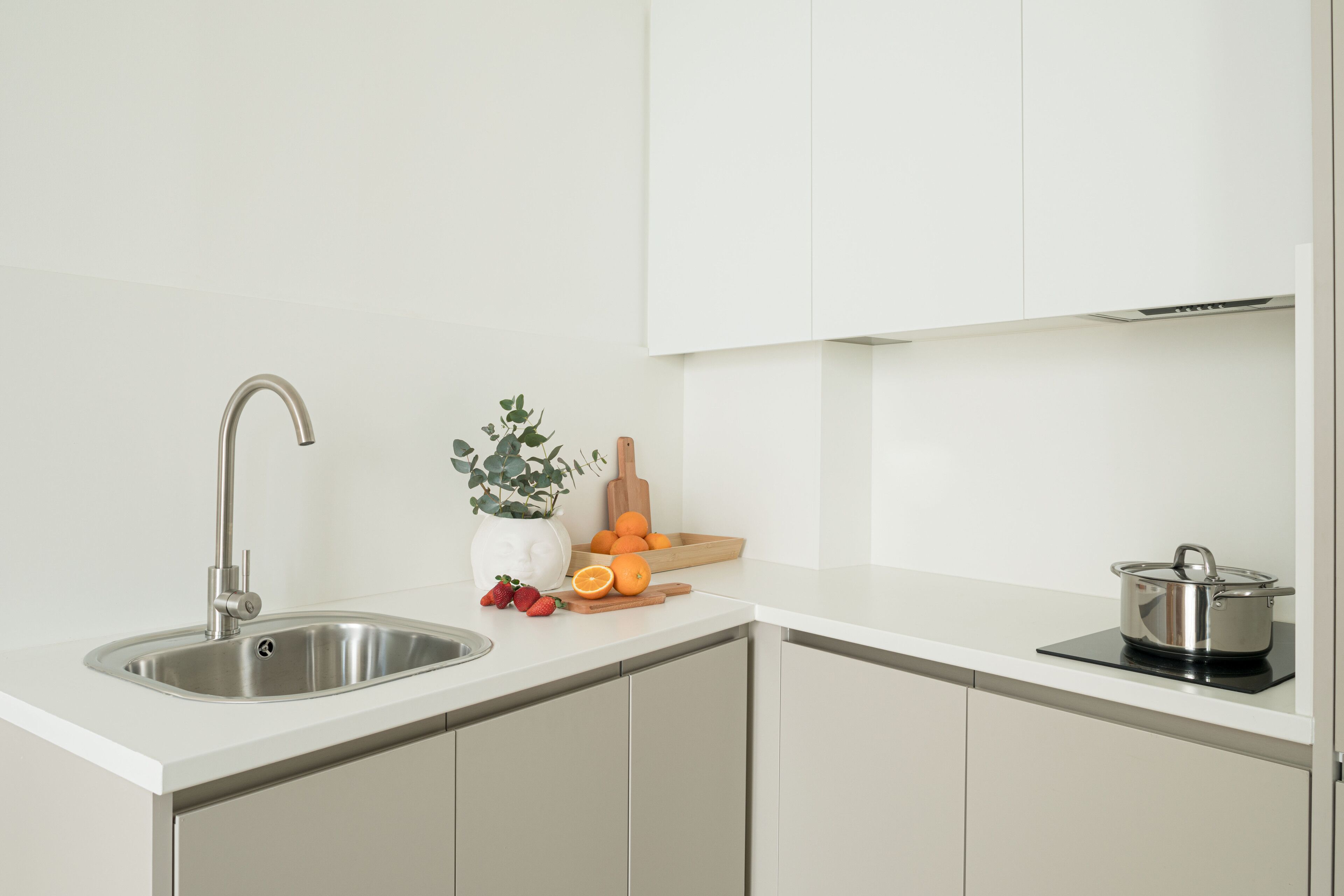 Een moderne keuken met een roestvrijstalen spoelbak, witte kasten, een potplant, een houten snijplank en een pan op een inductiekookplaat.