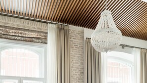 A modern living room with a wooden ceiling, a large white chandelier, wicker furniture, and a view of the city through large windows. - MYLU SUITES by PUERTA CATEDRAL (Seville)