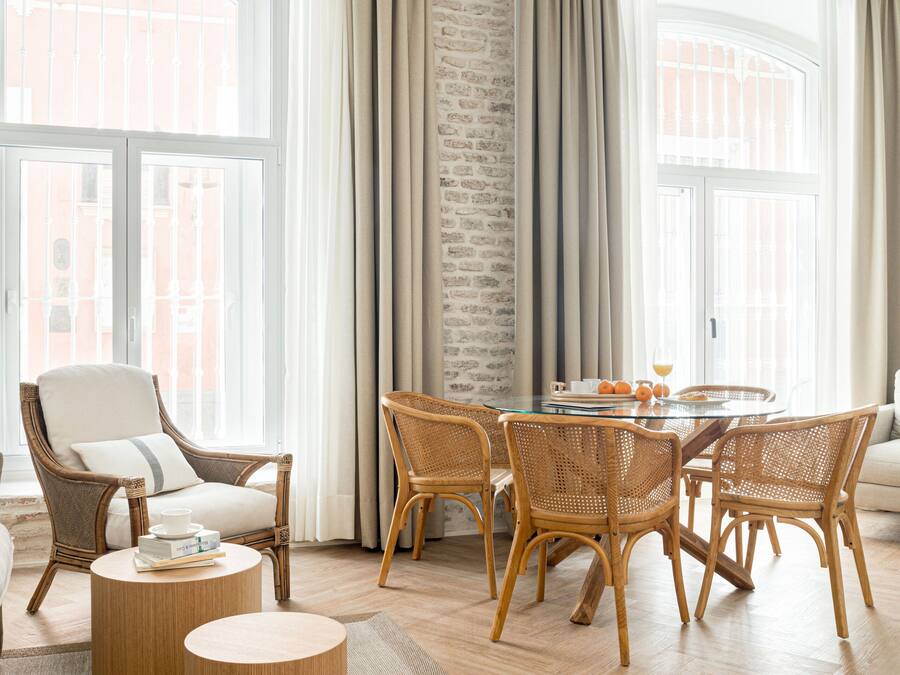 Un salon moderne avec un plafond en bois, un grand lustre blanc, des meubles en osier et une vue sur la ville grâce à de grandes fenêtres.