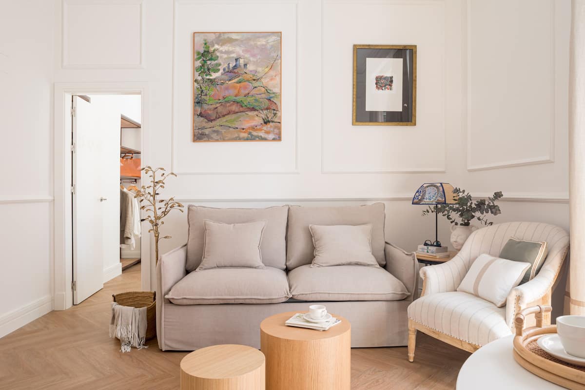A living room with a beige sofa, a round wooden coffee table, and a striped armchair.