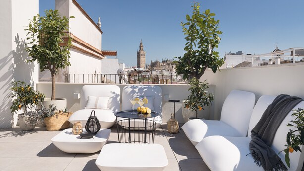 A rooftop terrace with white furniture, potted plants, and a view of a historic tower. - MYLU SUITES by PUERTA CATEDRAL (Seville)