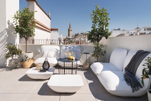 A rooftop terrace with white furniture, potted plants, and a view of a historic tower. - MYLU SUITES by PUERTA CATEDRAL (Seville)