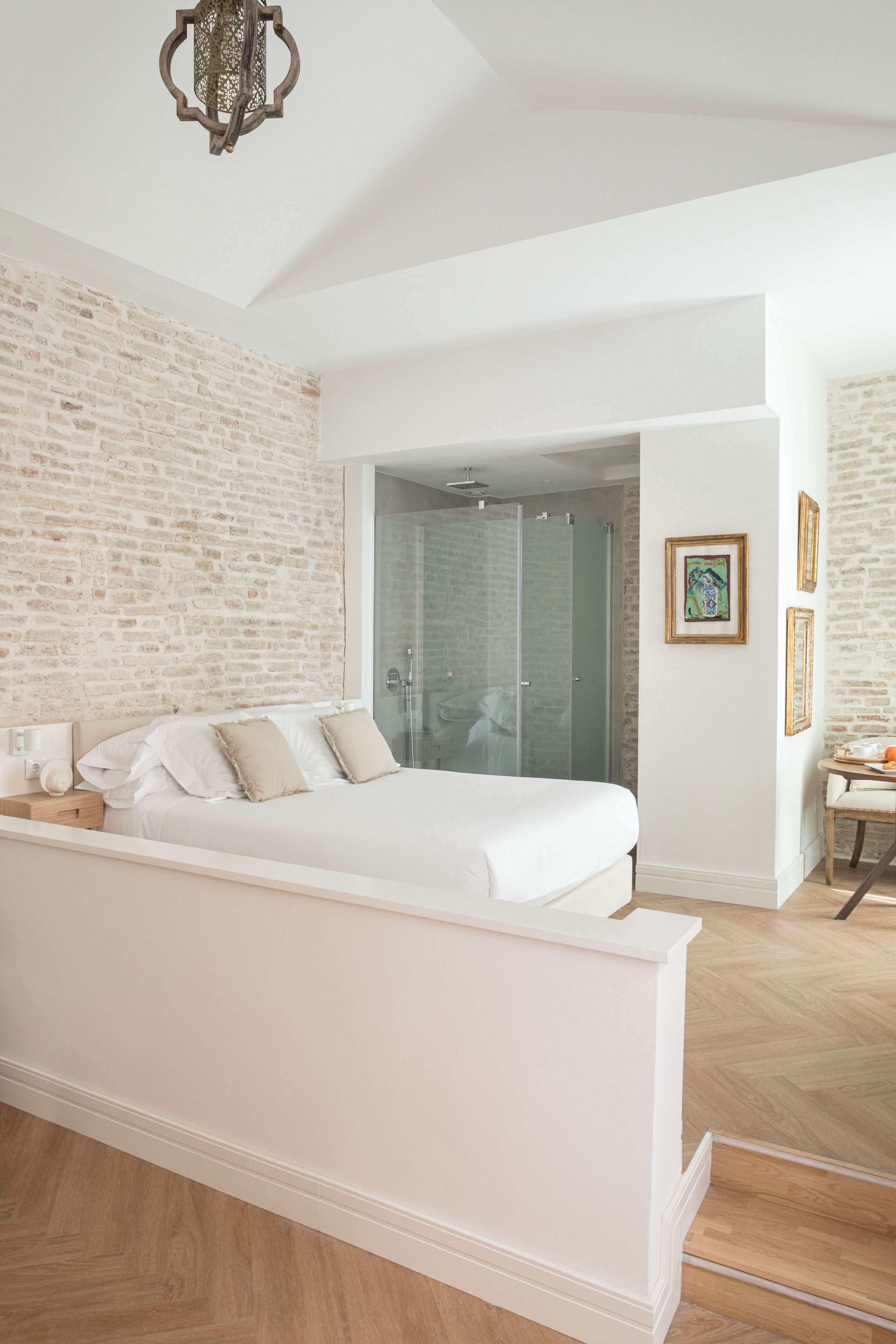 Une chambre avec un grand lit, une douche en verre et un mur en briques.