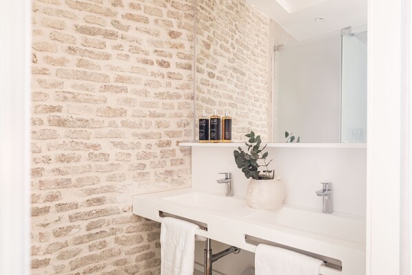 A bathroom with a brick wall, a white sink, a mirror, and a plant. - MYLU SUITES by PUERTA CATEDRAL (Seville)