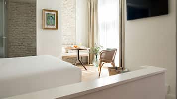 Une chambre d’hôtel avec un grand lit, un téléviseur fixé au mur, un coin repas avec une table et des chaises, et un mur en briques.