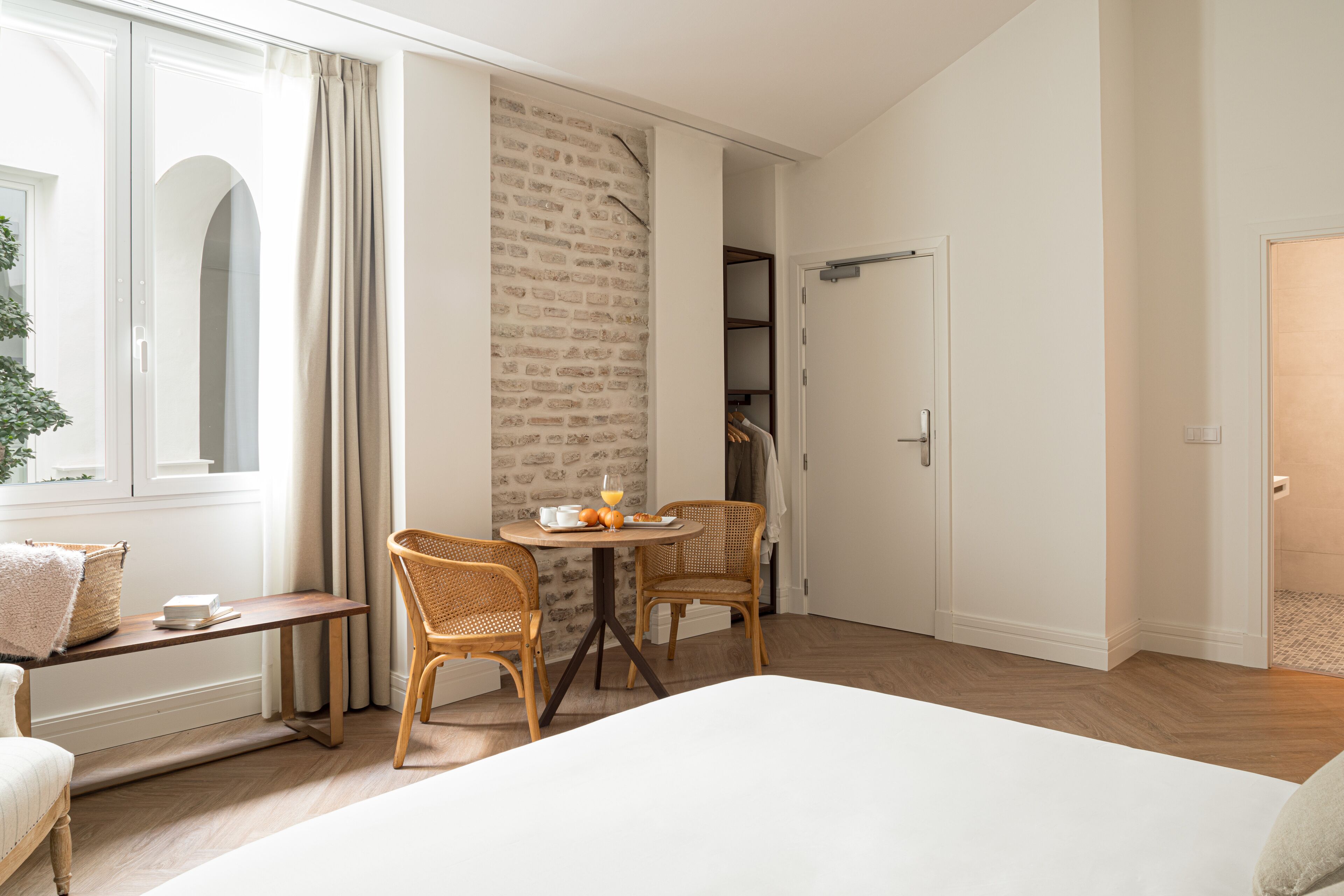 Ein Schlafzimmer mit einem großen Bett, einem Esstisch mit Stühlen, einem kleinen Tisch mit Orangensaft und einer Ziegelwand.
