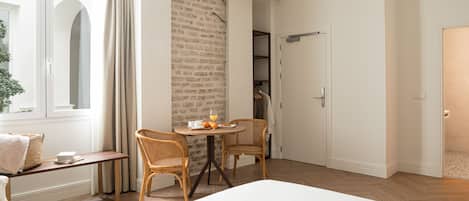 Ein Schlafzimmer mit einem großen Bett, einem Esstisch mit Stühlen, einem kleinen Tisch mit Orangensaft und einer Ziegelwand.