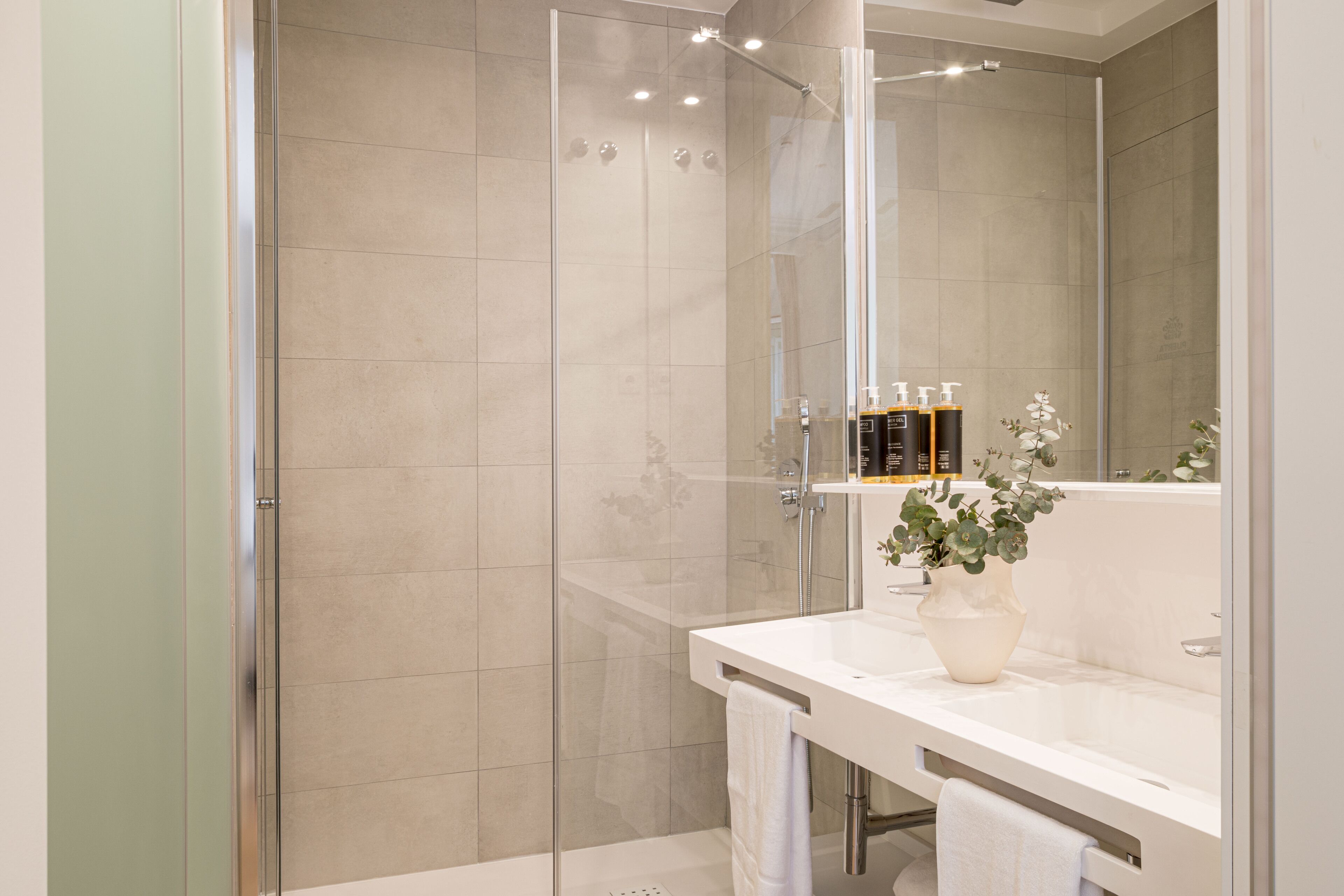 A modern bathroom with a glass-enclosed shower, a white sink, and a large mirror.