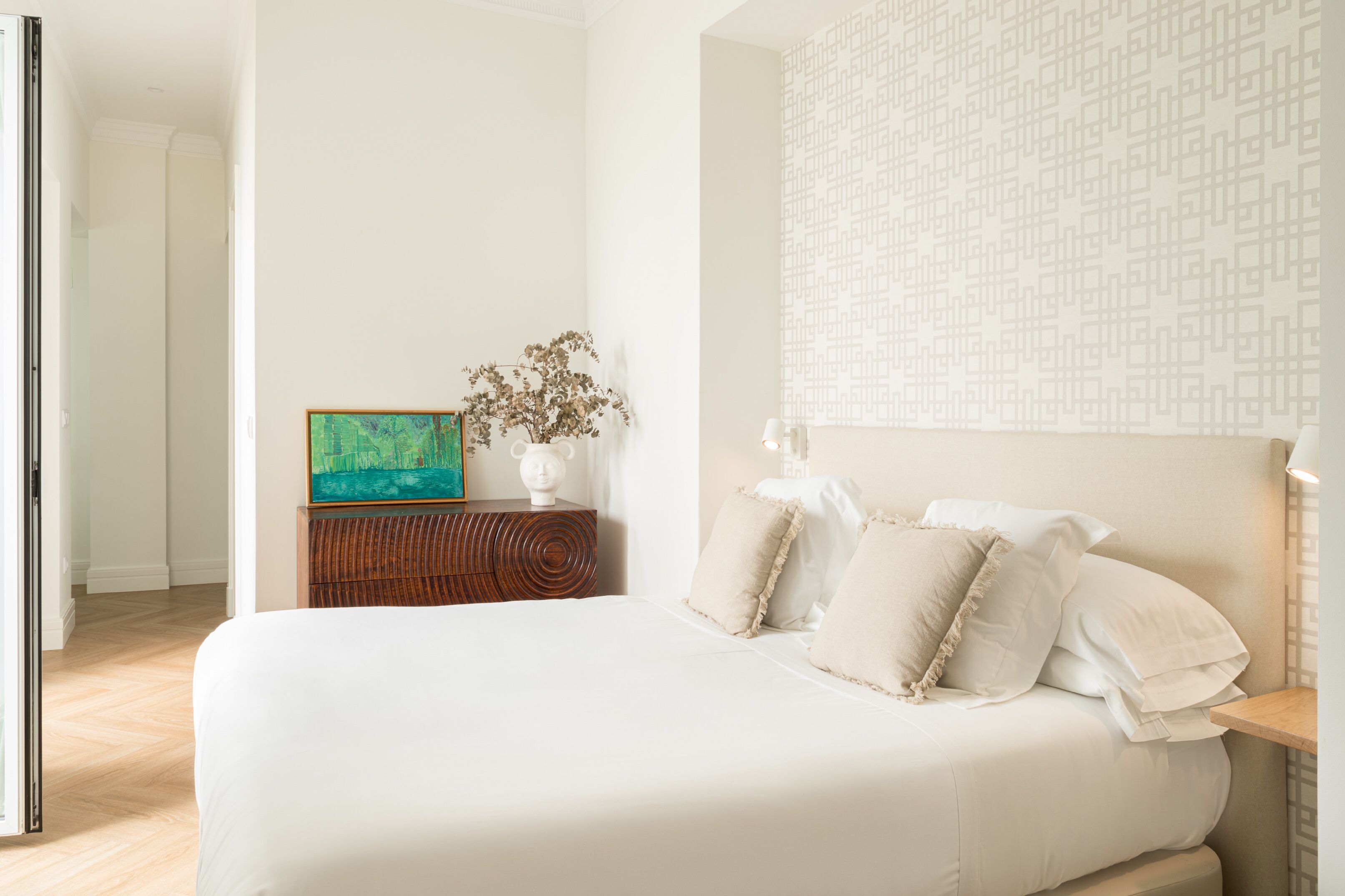 Un dormitorio ordenado con una cama grande, una mesita de noche con lámpara y una obra de arte colgada en la pared.