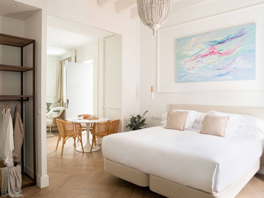A modern bedroom with a large bed, a dining area, and a hallway leading to another room.