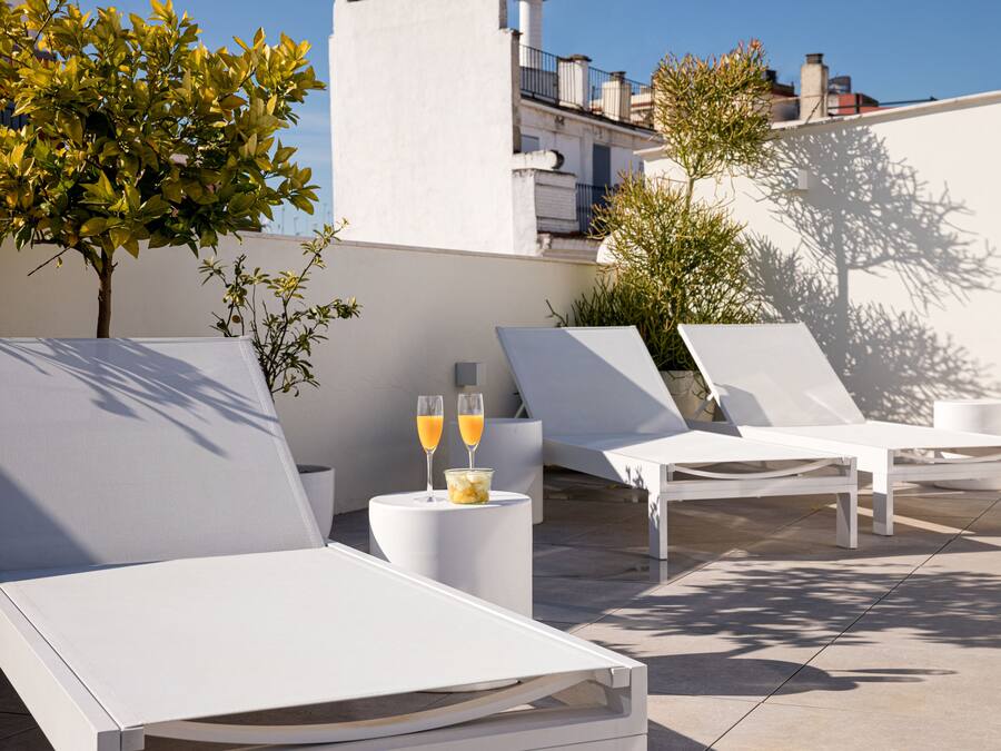 Een terras op het dak met witte lounge stoelen, een kleine tafel met twee glazen sinaasappelsap, en plantenpotten.