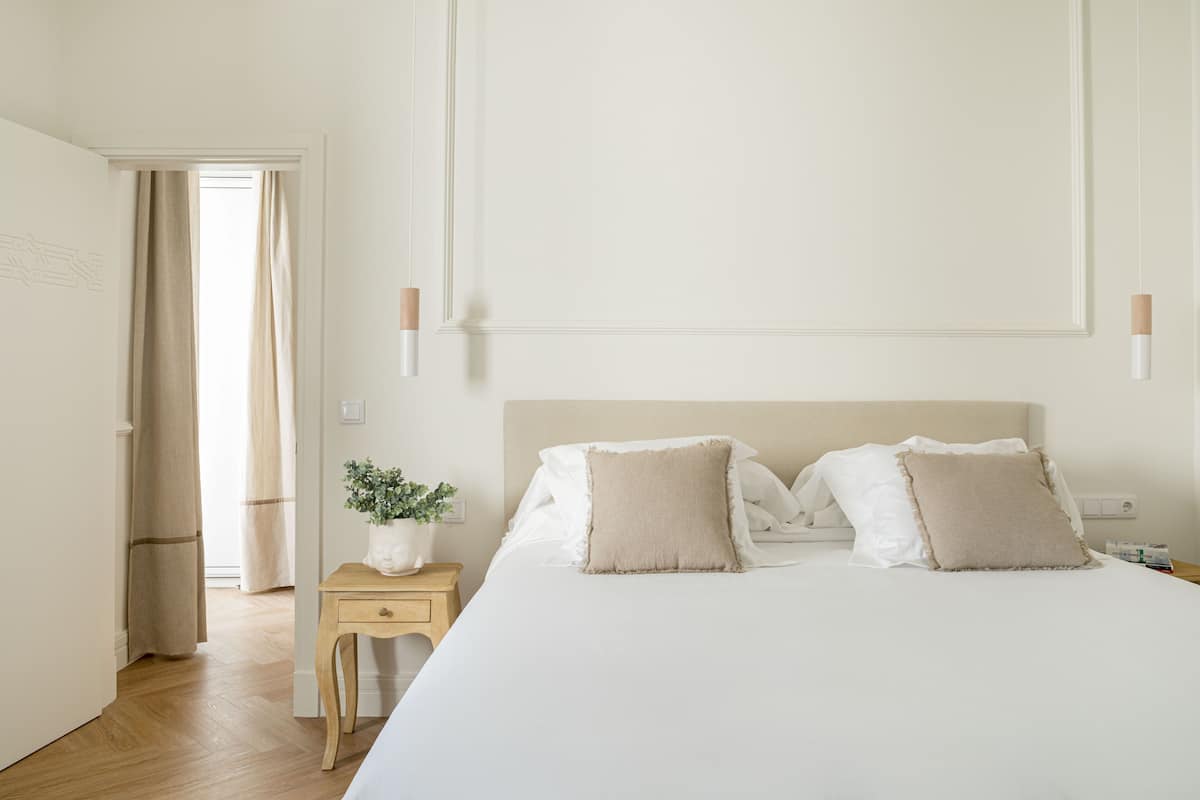 A bedroom with a bed, bedside table, lamp, and a potted plant.